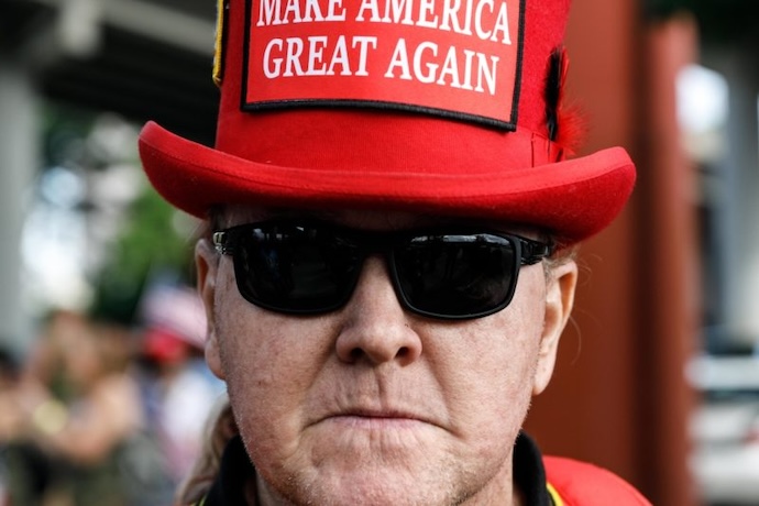 A far-right protestor wears a MAGA tophat with a grim expression.