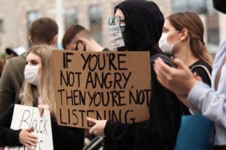 A person holding a sign that says "If you're not angry then you're not listening."