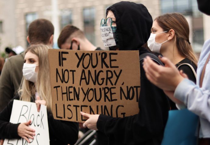 A person holding a sign that says "If you're not angry then you're not listening."