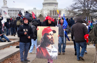 January 6 protester holds giant image of White Jesus in a Make America Great Again cap.