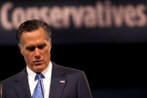 Image of Mitt Romney at a podium looking down with blurred sign in background that reads "Conservatives"