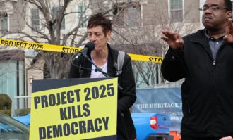 Two people on a podium with a board that reads "Project 2025 kills democracy"
