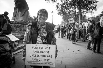 Anti-Zionist Jewish Protestor holds sign "you are not antiracist unless you are anti-zionist"